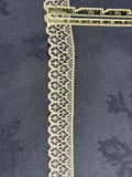 Ivory flat lace trim 25mm wide with scalloped edge and open geometric pattern, shown on denim fabric with a ruler for scale