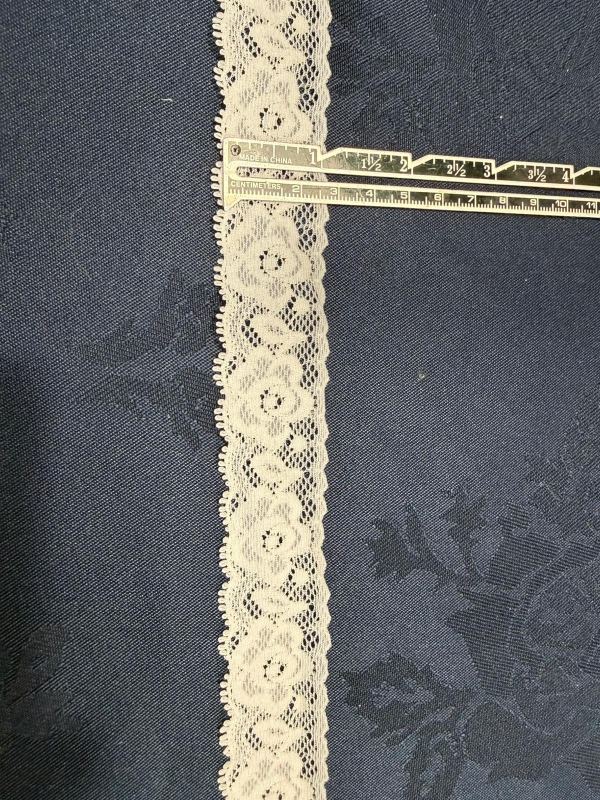 Ivory stretch lace trim 30mm wide with circular floral pattern and picot edges, shown on denim fabric with a ruler for scale
