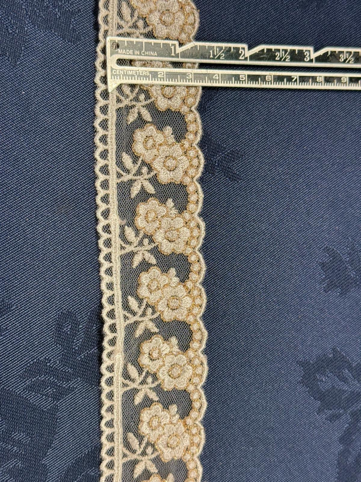 Cream and gold embroidered tulle lace 40mm wide with raised floral and leaf pattern and scalloped edge, shown on denim fabric with a ruler for scale