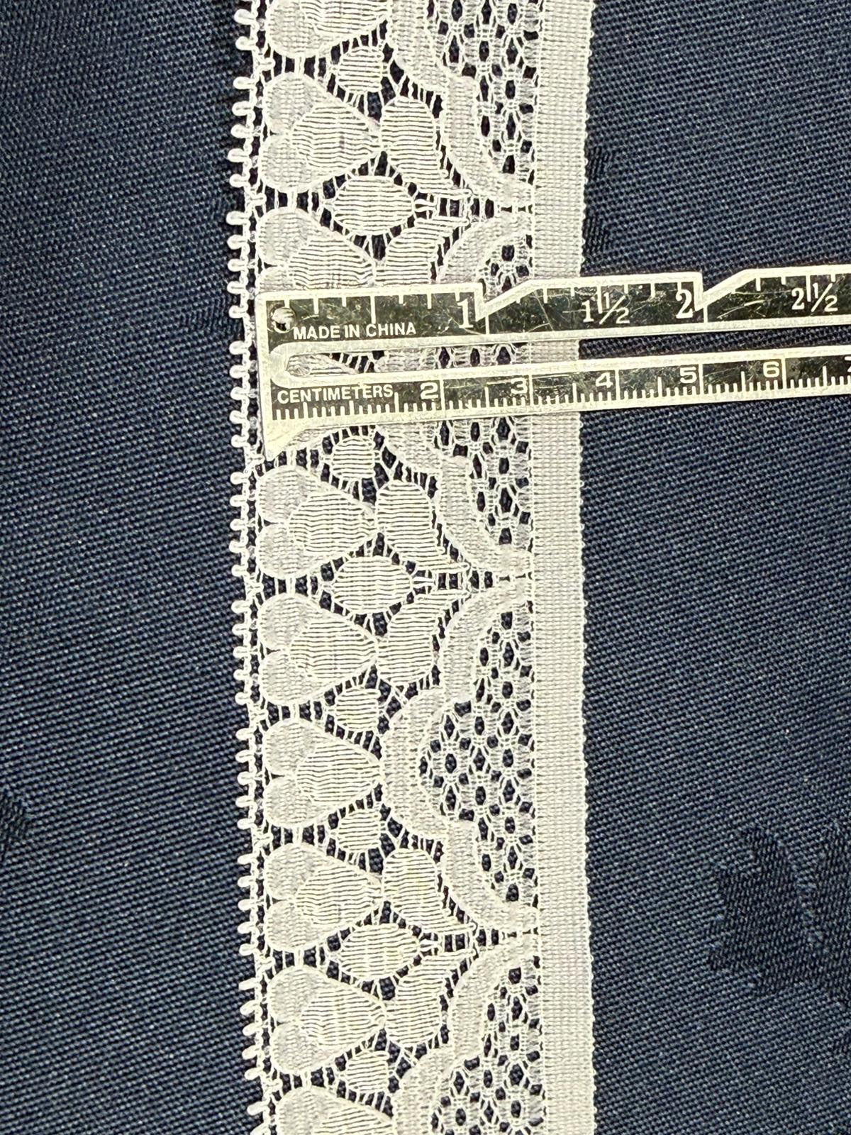 White flat lace trim 20mm wide with open floral pattern and picot edges, shown on denim fabric with a ruler for scale