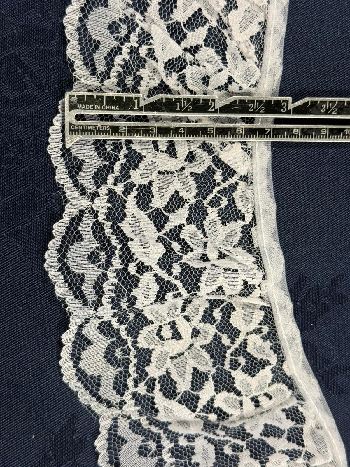 White gathered lace trim 80mm wide with full floral and leaf pattern and scalloped edge, shown on denim fabric with a ruler for scale